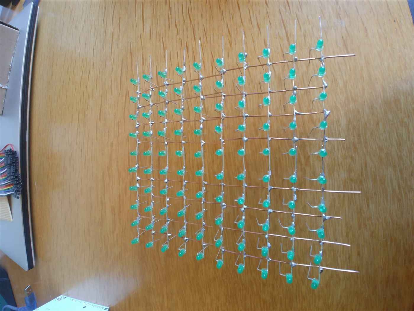 Ten rows of green LEDs soldered into a square grid on a workbench