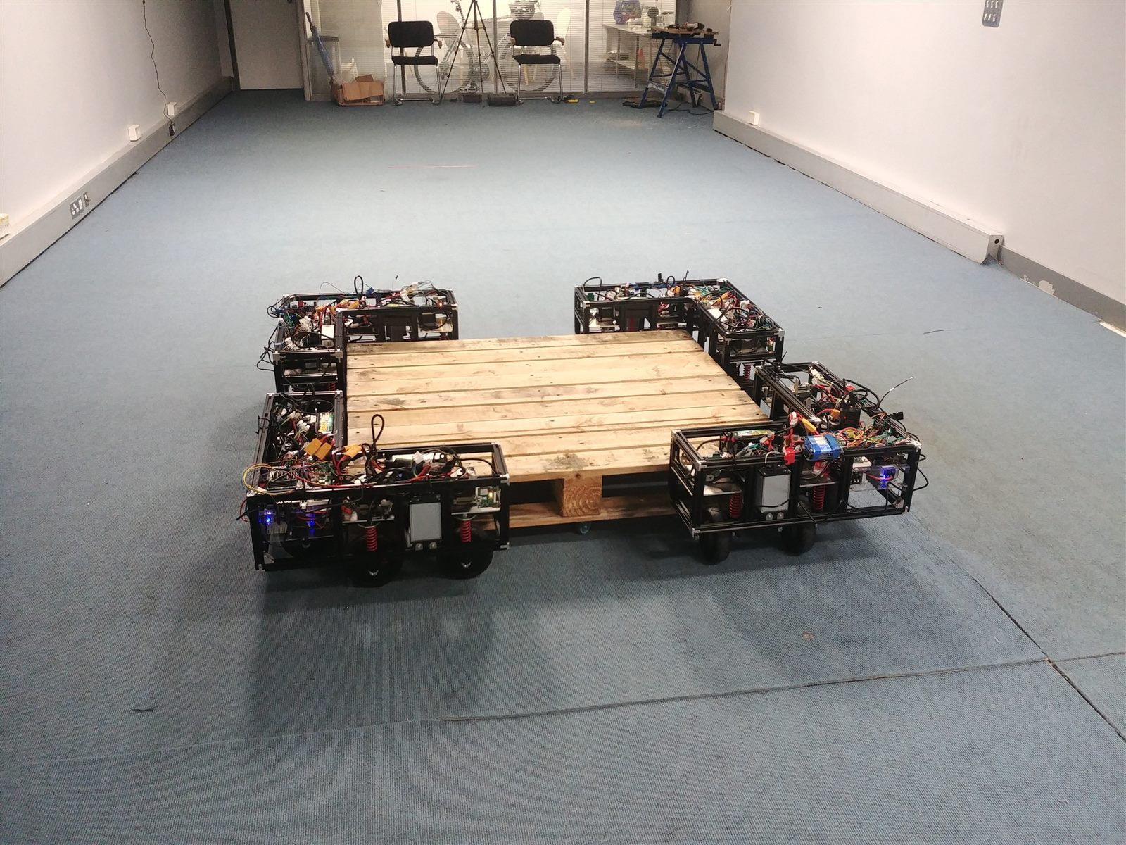 Four autonomous robots positioned around a wooden pallet during a multi-robot test